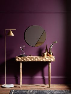 a wooden table with a mirror and vase on it in front of a purple wall