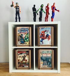 some action figures are sitting on top of a book shelf in front of a wall