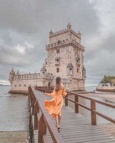 a woman in an orange dress is walking on a bridge over the water near a castle