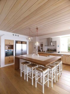 a large kitchen with wooden floors and white walls, has an island table surrounded by stools