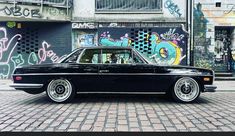 an old black car parked in front of a graffiti covered building with white rims