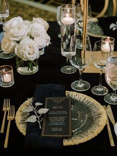 a black table cloth with white flowers and silverware on it is set for a formal dinner