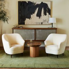 two white chairs sitting next to each other in front of a painting on the wall