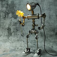 a metal robot holding a yellow flower in its hand and looking at it's surroundings