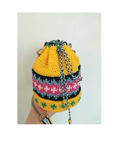 a woman's hand is holding a yellow crocheted bag with chains on it