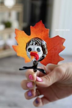 a hand holding an orange and red leaf with a turkey face on it's head