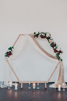 a wedding arch with candles and flowers on the side is decorated with white sheer fabric