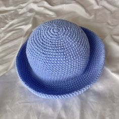 a blue crocheted hat laying on top of a white bed sheet with sheets