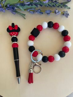 a red, white and black beaded bracelet with mickey mouse keychain next to a pen