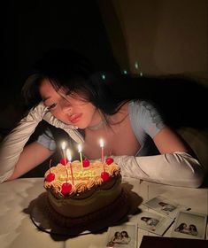 a woman sitting in front of a cake with lit candles on it and looking down