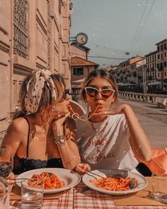 two women sitting at a table with plates of spaghetti in front of them, eating