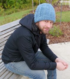 a man sitting on top of a wooden bench wearing a blue knitted beanie