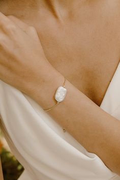 a woman wearing a white dress with a gold bracelet on her arm and a pearl bead around the wrist