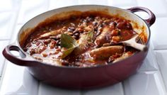 a red pot filled with meat and beans on top of a white tile countertop