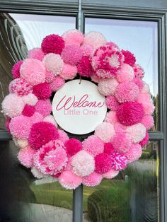 a pink and white wreath with the words welcome little one on it