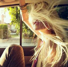 a woman sitting in the back seat of a car with her hair blowing in the wind