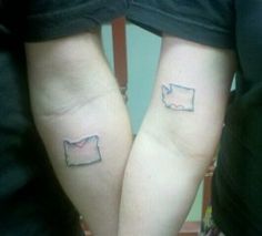 two people with matching tattoos on their arms, one has a heart and the other has a map