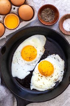 two fried eggs in a skillet next to other ingredients