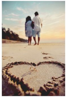 two people standing in the sand with a heart drawn in the sand