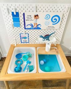 two trays filled with water and toys on top of a wooden table in front of a white wall