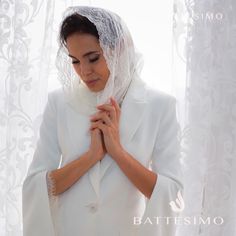 a woman wearing a white veil and holding her hands together in front of a window