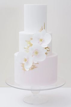 a three tiered cake with white and gold flowers on the top, sitting on a glass plate