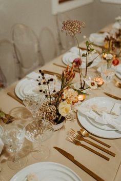 the table is set with plates, silverware and flowers in vases on it