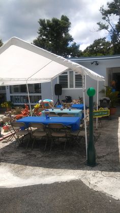 a table and chairs under a white tent with blue cloths on it in front of a house