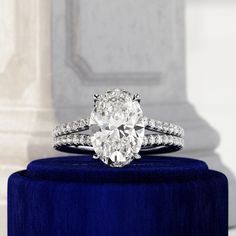 an oval cut diamond ring sits on top of a blue velvet stand in front of a pillar