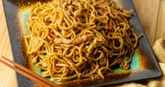 a plate of noodles with meat and chopsticks on the side, ready to be eaten