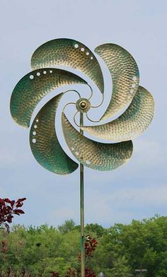 a large metal wind spin sitting on top of a lush green field