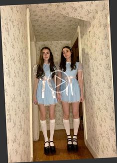 two young women dressed in short blue dresses are standing in an open doorway and looking at the camera