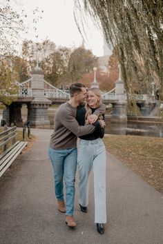 a man and woman walking down a path in front of a bridge holding each other