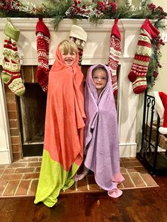 two children wrapped in blankets standing next to a fireplace