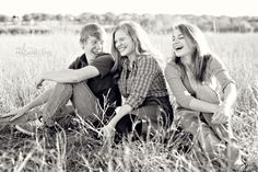 two women and a boy sitting in the middle of a grassy field with their arms around each other