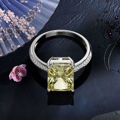 a fancy yellow diamond ring on a black surface with an umbrella and flowers in the background