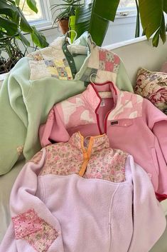 several pink and green sweaters sitting on top of a white couch next to a potted plant