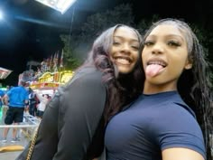 two women standing next to each other in front of a carnival ride with their tongue hanging out