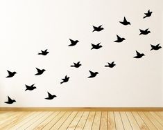 a flock of birds flying in the air on a white wall above a wooden floor