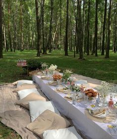 a long table is set up in the woods for an outdoor picnic party with food and drinks on it