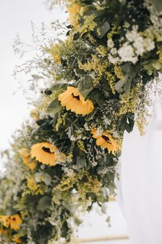 yellow flowers and greenery are arranged on the back of a large white urn