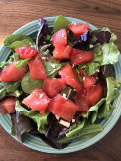 a salad with watermelon and lettuce in a blue bowl on a wooden table