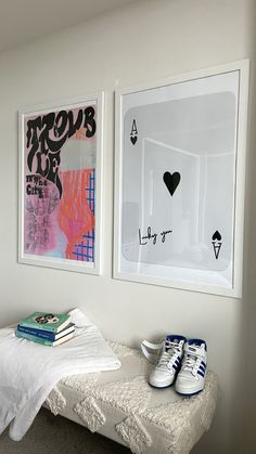 two paintings hang on the wall next to a bed with white sheets and blue sneakers