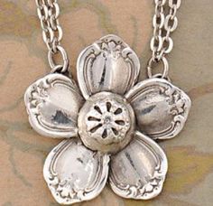 a silver flower necklace on a chain with an image of the flower in the center