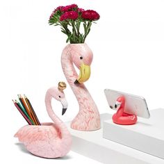 a pink flamingo sitting on top of a white shelf next to a vase filled with flowers