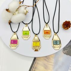 four necklaces with different colored stones on a white plate next to a cotton ball