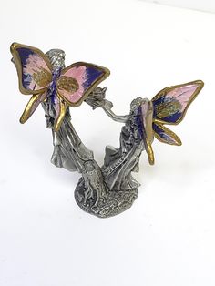 two metal figurines with pink and blue butterflies on their backs, one holding the other's hand