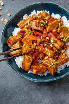 a blue bowl filled with chicken and rice on top of a table next to chopsticks