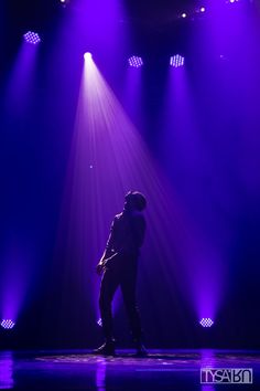 a man standing on top of a stage in front of purple lights and spotlights