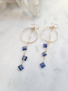 Evening Bloom Earrings featuring the amazing blue of Kyanite! Available in Sterling Silver or 14K Gold Filled. Each hoop is hand formed and hammered for texture and shape. Three beautiful diamond shaped Kyanite Gems dangle from a cable chain on each earring. The length of the earrings are approx. 2 3/4 in. Each piece is handmade and may vary slightly as well as the stones as they are natural. They will vary in size and color. Kyanite gemstone is amazing as it does not hold on to nor retain negative energy. It is said to bring calm and peace to stressful times. It stimulates the throat chakra to help with communication of all kinds. Thank you for your support! Kyanite Earrings, Gemstone Hoop Earrings, Dangle Hoop Earrings, Blue Kyanite, Diamond Shaped, Cable Chain, Gemstone Earrings, Diamond Shapes, Sterling Silver Earrings